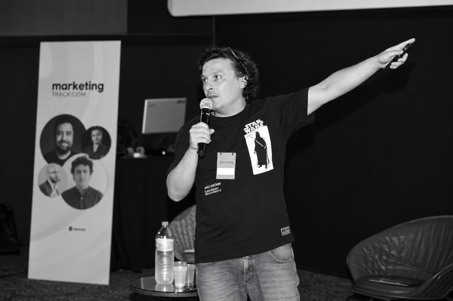 Fernando D’Angelo em uma palestra, falando ao microfone e apontando para a plateia